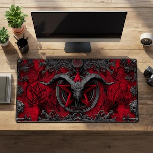May include: A rectangular red and black desk mat featuring a central pentagram design with a goat skull, surrounded by ornate scrollwork. Two pentagrams are on either side of the central design. The mat is on a wooden desk with a computer monitor and plants.