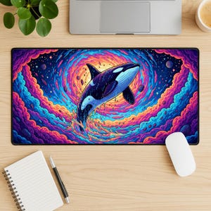 May include: A rectangular black mousepad featuring a vibrant illustration of a killer whale leaping from swirling, colorful clouds. The whale is primarily dark blue with white markings, set against a backdrop of swirling blues, purples, and oranges.