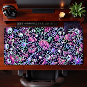May include: A large, rectangular mousepad featuring a vibrant, surreal design of brains, eyeballs, and neural networks in shades of purple, pink, and green against a black background. The mousepad is placed on a wooden desk.