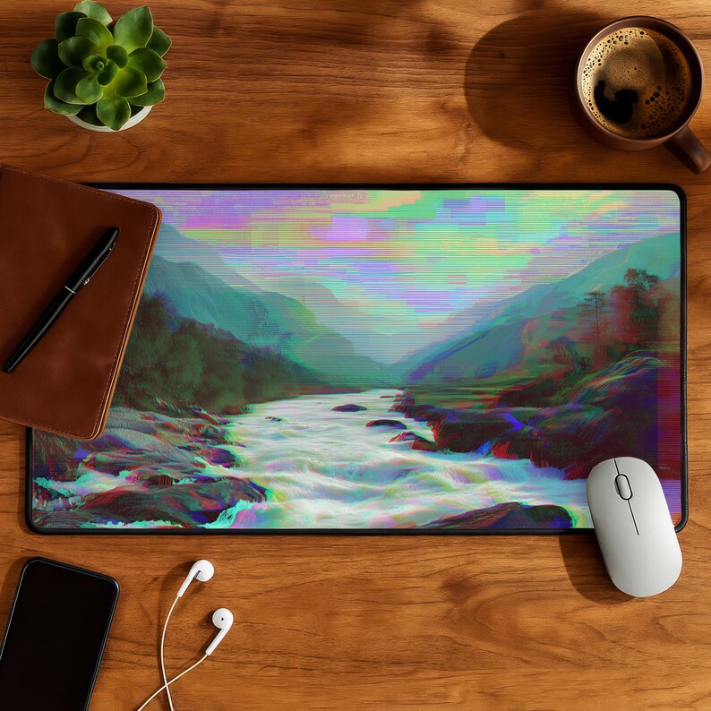 Peut inclure: Tapis de souris rectangulaire avec un paysage d'art num&eacute;rique d'une rivi&egrave;re traversant des montagnes, avec un effet de glitch. Le tapis est noir avec une souris blanche et est sur une surface en bois. Un carnet en cuir marron, un stylo et une tasse de caf&eacute; sont &eacute;galement visibles.