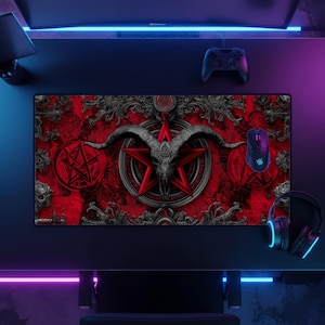May include: A rectangular gaming mouse pad with a red background and a black goat skull design. The design includes a pentagram and ornate scrollwork. A black mouse, controller, and headset are also visible.