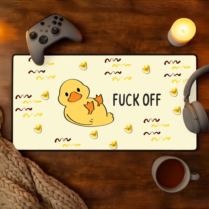 May include: A rectangular mousepad with a yellow background featuring a cartoon duck and the words "FUCK OFF" in black. The design includes yellow duck footprints and brown wavy lines. A gray game controller and headphones are visible.