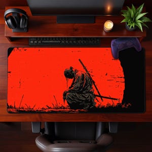 May include: A large rectangular mouse pad featuring a red background with a black silhouette of a samurai kneeling with two swords. The design is a stylized illustration with a dark, dramatic aesthetic.