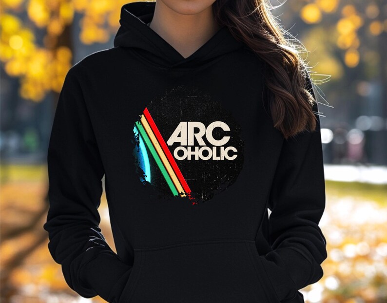 Puede incluir: Una sudadera con capucha negra que presenta un gr&aacute;fico circular en el pecho. El dise&ntilde;o incluye el texto ARC OHOLIC en letras may&uacute;sculas blancas, acompa&ntilde;ado de tres rayas diagonales en azul, verde y rojo sobre un fondo negro desgastado.