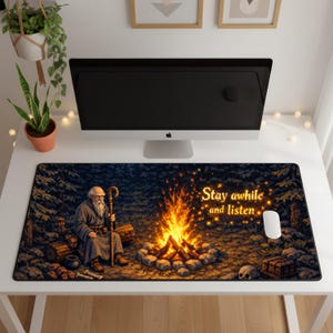 Puede incluir: Alfombrilla de rat&oacute;n rectangular con una escena de bosque, una fogata y un anciano con un bast&oacute;n. El texto "Stay awhile and listen" est&aacute; en dorado. Un rat&oacute;n de ordenador est&aacute; a la derecha.