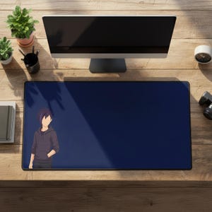 Puede incluir: Una alfombrilla de escritorio rectangular azul marino con una ilustración de estilo anime de una persona con una sudadera con capucha gris. La alfombrilla está sobre un escritorio de madera, con un monitor de ordenador, plantas y otros suministros de oficina.