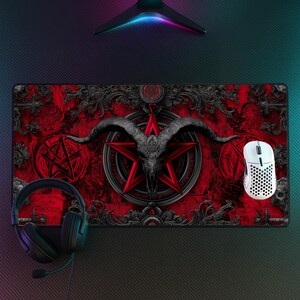 May include: A rectangular red and black gaming mousepad featuring a pentagram, goat skull, and ornate scrollwork design. A white wireless mouse and black headset are on the right and left sides of the pad, respectively.