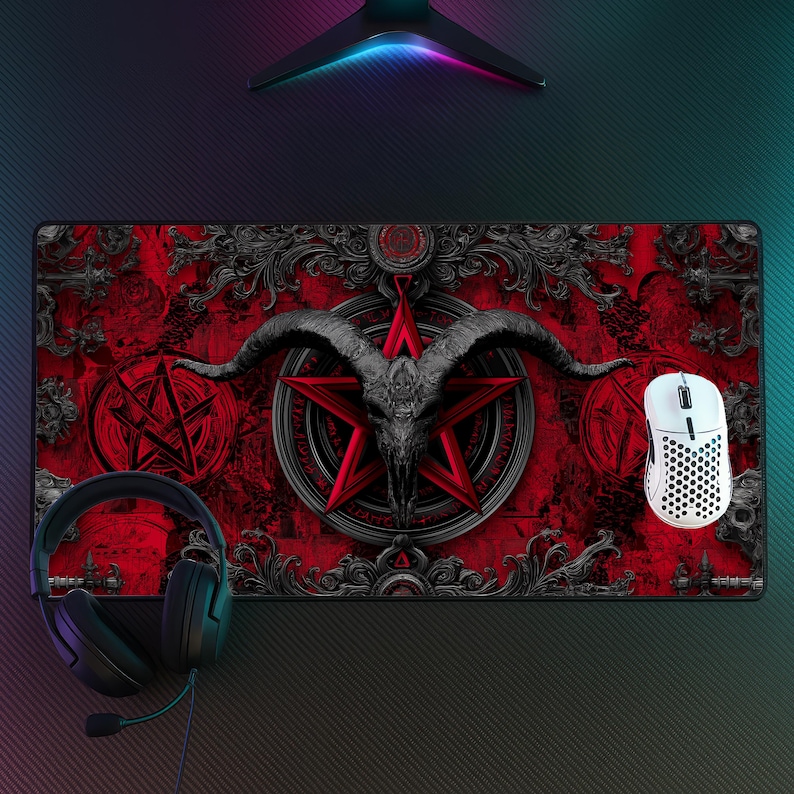 May include: A rectangular red and black gaming mousepad featuring a pentagram, goat skull, and ornate scrollwork design. A white wireless mouse and black headset are on the right and left sides of the pad, respectively.