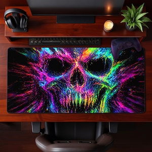 May include: A large rectangular desk mat featuring a vibrant, colorful skull design. The skull is rendered in shades of purple, blue, green, and yellow against a black background. The mat is designed for use with a computer and accessories.