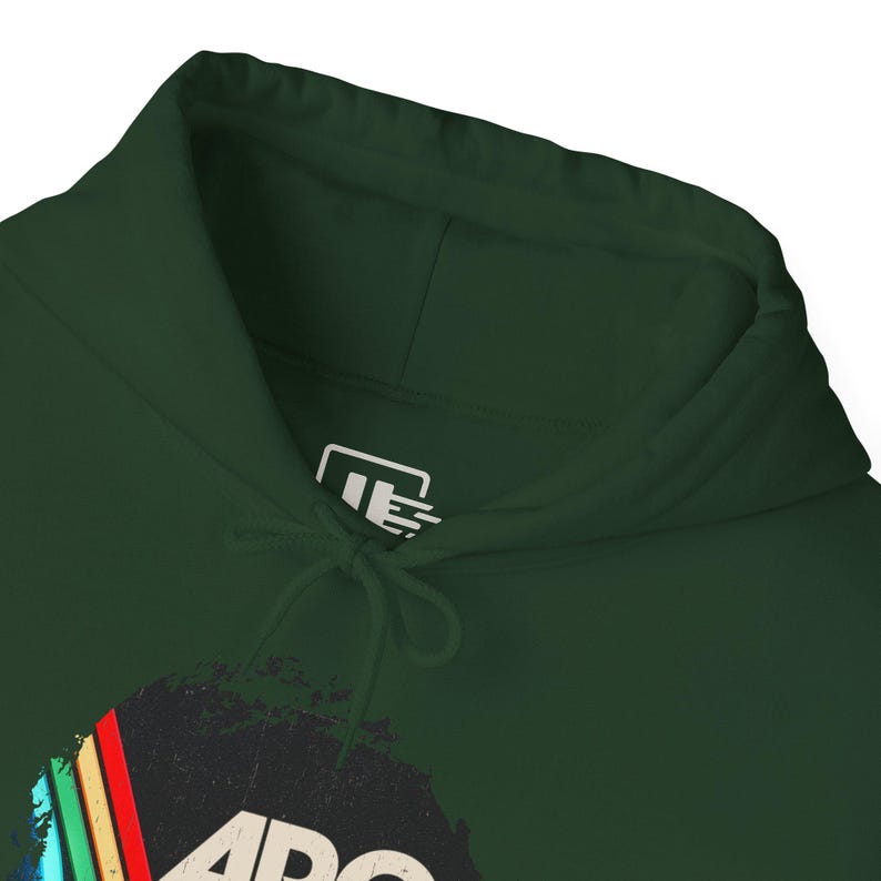 Puede incluir: Una sudadera con capucha de color verde bosque oscuro con cord&oacute;n ajustable. La etiqueta interior del cuello presenta un logotipo gr&aacute;fico blanco con las letras JE. Un estampado gr&aacute;fico parcial es visible en la parte inferior, mostrando rayas diagonales coloridas.