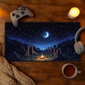 Könnte beinhalten: Rechteckiges Mauspad mit einer Pixel-Art-Nachtszene, die einen Halbmond, Sterne und ein Lagerfeuer zeigt. Ein grauer Gamecontroller und Kopfhörer befinden sich auf der Holzoberfläche. Eine brennende Kerze und eine Tasse Tee sind ebenfalls vorhanden.