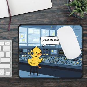 Op de afbeelding: Een rechthoekige muismat met een gele cartoon-eend met een headset, zittend op een kruk voor een complexe bedieningsconsole met veel knoppen en schermen. Een tekstballon bevat de tekst DOING MY BEST.