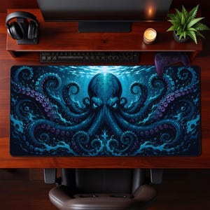 Könnte beinhalten: Eine rechteckige Schreibtischunterlage mit einem großen, dunkelblauen Oktopus mit leuchtenden Augen und wirbelnden Tentakeln, umgeben von turbulentem Wasser. Das Motiv ist mittig auf der Unterlage platziert, die auf einem dunklen Holzschreibtisch unter einem Monitor, einer Tastatur und einem Controller liegt.