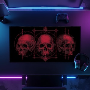 May include: A rectangular desk mat featuring a black background with three detailed red skulls arranged horizontally. The design includes intricate geometric lines, circular patterns, and occult-inspired symbols surrounding the skulls in a dark aesthetic.