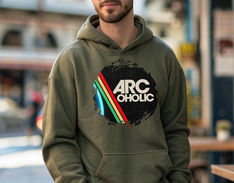 Puede incluir: Una sudadera con capucha de color verde oliva que presenta un gr&aacute;fico circular en el pecho. El dise&ntilde;o incluye un c&iacute;rculo negro desgastado con el texto blanco ARC OHOLIC y tres rayas diagonales en azul, amarillo y rojo. Tiene un bolsillo frontal.