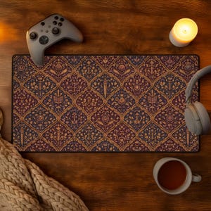 May include: A rectangular mousepad with a detailed, repeating pattern in shades of burgundy, blue, and gold. The design features stylized swords, books, and other ornate elements. A gray game controller, headphones, and a cup of tea are also visible.