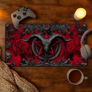 May include: A red and black gaming mousepad featuring a goat skull within a red pentagram. The design includes ornate, gothic-style borders and pentagrams. A gray game controller, headphones, and a lit candle are visible.