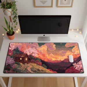 以下が含まれることがあります： 小屋、木々、夕焼けを描いたピクセル化された風景が特徴の長方形のマウスパッド。カラーパレットにはピンク、オレンジ、紫の色合いが含まれています。白いマウスがパッドの右側にあります。