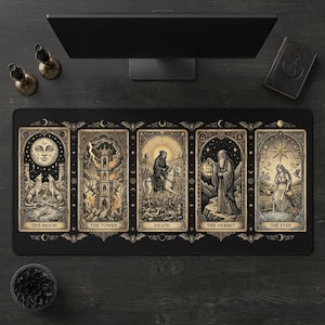 Puede incluir: Alfombrilla de escritorio rectangular negra con ilustraciones de cartas del tarot. La alfombrilla muestra cinco cartas: La Luna, La Torre, La Muerte, El Ermitaño y La Estrella. Cada carta tiene bordes ornamentados y su título. El diseño es en beige y negro.