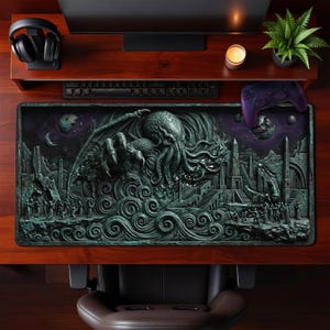 Puede incluir: Una alfombrilla de escritorio rectangular con una ilustración en relieve de color verde azulado oscuro que muestra una criatura con tentáculos emergiendo de olas turbulentas. Incluye ruinas antiguas, obeliscos y figuras en costas rocosas.