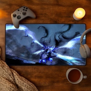 Op de afbeelding: Een rechthoekige bureaumat met een donkere, etherische figuur met gloeiende blauwe vleugels en wervelende, rookachtige ranken. De mat wordt omringd door een grijze draadloze gamecontroller, lichtgrijze koptelefoon, een witte kaars en een mok.