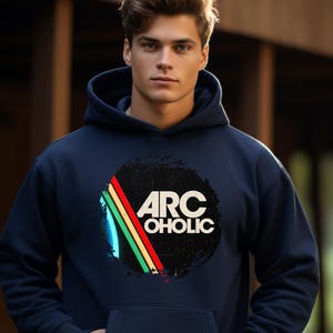 Puede incluir: Una sudadera con capucha azul marino que presenta un gr&aacute;fico circular en el pecho. El dise&ntilde;o incluye el texto ARC OHOLIC en blanco, sobre un c&iacute;rculo negro desgastado con tres rayas diagonales en amarillo, verde y rojo a la izquierda.
