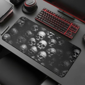 May include: A black rectangular mousepad featuring a repeating pattern of grayscale skulls. The mousepad is positioned on a dark surface, alongside a black keyboard with red backlighting and other computer accessories.