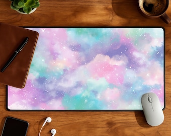 May include: A rectangular mouse pad with a colorful galaxy design in shades of pink, purple, and teal. The pad is surrounded by a black border. A white mouse, a smartphone, and a pair of headphones are on the wooden surface.