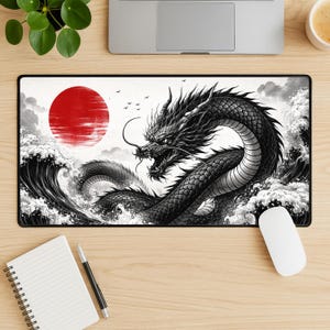 Könnte beinhalten: Schwarzes rechteckiges Mauspads mit einer detaillierten Illustration eines schwarzen Drachen inmitten von tosenden Wellen und einer roten Sonne. Das Design ist von traditioneller japanischer Kunst inspiriert. Eine weiße Computermaus befindet sich rechts.