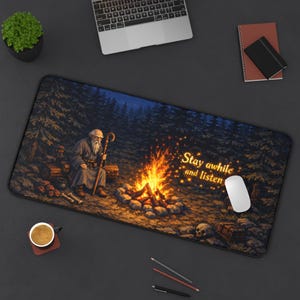 Puede incluir: Alfombrilla de escritorio rectangular con una ilustraci&oacute;n de un anciano junto a una fogata en un bosque. El texto "Stay awhile and listen" est&aacute; a la derecha. Un rat&oacute;n de ordenador est&aacute; sobre la alfombrilla.