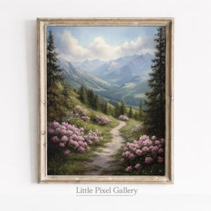May include: A framed landscape painting depicts a mountain scene with a path winding through a field of pink flowers. The artwork features a light blue sky with fluffy clouds and a distant mountain range. The painting is signed "Little Pixel Gallery".