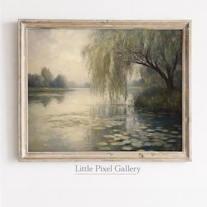 May include: A framed landscape painting depicts a serene waterscape with a weeping willow tree. The artwork features soft, muted tones of green, beige, and gray, with lily pads floating on the water's surface. The frame is a light, distressed wood.
