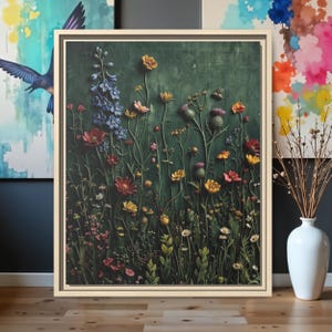 Puede incluir: Una obra de arte enmarcada que presenta un relieve texturizado de flores silvestres en tonos amarillos, rojos, rosas y azules sobre un fondo verde oscuro. La obra de arte se presenta en un marco de madera de color claro.