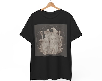 Op de afbeelding: Zwart t-shirt met een sepia-kleurige illustratie van twee tovenaars met lange baarden en puntmutsen, omringd door paddenstoelen en bladeren. De tovenaars houden staven vast. Het ontwerp is geplaatst in een cirkelvormig kader.