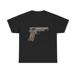 Op de afbeelding: Zwart t-shirt met een gedetailleerde illustratie van een handvuurwapen. Het pistool heeft ingewikkelde gravures en een bruine grip. Het ontwerp is gecentreerd op het shirt en biedt een opvallende uitstraling.