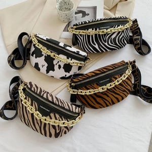 May include: Four animal print fanny packs with gold chain detailing and black zippers. One has a cow print, another a zebra print, and two feature tiger stripes. Each bag has an adjustable strap and the text "FASHION & BAG".