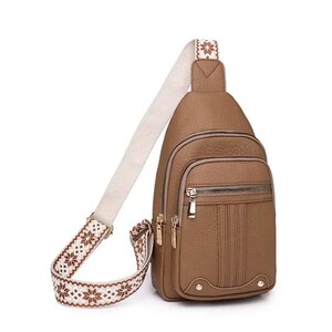 May include: A brown sling bag with a cream-colored strap featuring a geometric pattern in brown and white. The bag has multiple zippered compartments and gold-colored hardware. The bag is approximately 12 inches tall.