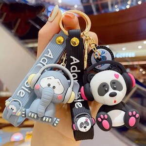May include: A collection of keychains featuring cartoon animals wearing headphones. The keychains include a gray elephant, a panda bear, and a small cloud. The keychains have the word "Adorable" and "Adorable" printed on the straps.