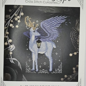 May include: A cross-stitch pattern titled "Winter Peryton" featuring a mythical creature with deer-like features, wings, and a lantern. The design is in shades of blue and white, with gold accents. The text "The Stitch Crypt" is at the top.