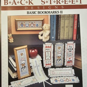 May include: A craft pattern book titled "Back Street Designs Basic Bookmarks II" featuring cross-stitch bookmark designs. Designs include framed pictures, a stack of books, and various bookmark styles with text and images.