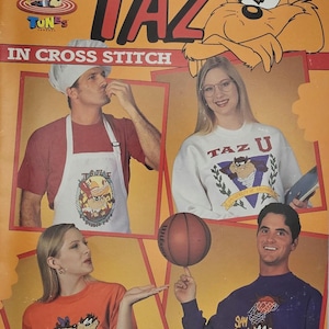May include: A vintage Looney Tunes cross-stitch pattern leaflet featuring Taz. The cover displays images of people wearing Taz-themed apparel, including t-shirts, a sweatshirt, and an apron. The leaflet includes the text "TAZ" in large red letters.