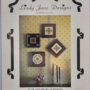 May include: A page from "Lindy Jane Designs" featuring framed cross-stitch patterns. The designs include floral motifs in square and diamond frames, displayed against a patterned wallpaper. The title "TULIP AND HEART SYMPHONY" is visible.
