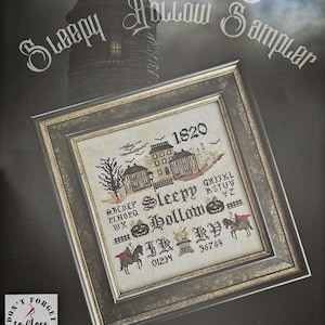 May include: Framed cross-stitch sampler titled "Sleepy Hollow" with a spooky theme. The design features a haunted house, pumpkins, and a headless horseman. The text includes "1820" and the words "Sleepy Hollow Sampler". The frame is a dark metallic color.