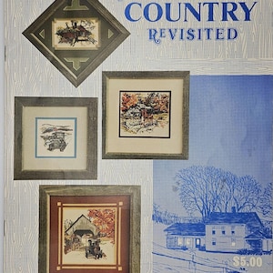 May include: A collection of framed cross-stitch artworks featuring rural scenes. The frames are various shapes and sizes, with a rustic aesthetic. The artwork includes images of a covered bridge, a horse-drawn carriage, and a landscape with trees. The title "Puckerbrush Country Revisited" is displayed.