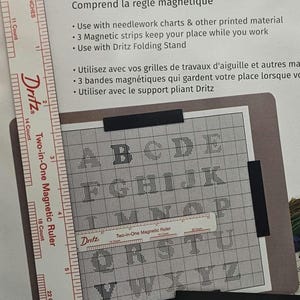 May include: An 8" x 10" magnet board set with a magnetic ruler. The set includes a magnetic ruler, magnetic strips, and a folding stand. The board displays the alphabet in a grid pattern, ideal for needlework.