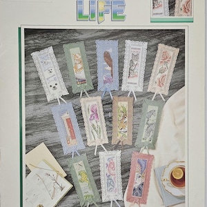 May include: A collection of decorative bookmarks with various designs, including animals, flowers, and portraits. Each bookmark features a detailed image within a lace-trimmed frame and a ribbon. The text "SLICE OF LIFE" is displayed at the top.