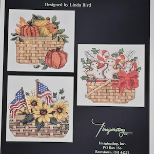 May include: A cross-stitch pattern booklet titled Seasonal Baskets 1910 designed by Linda Bird. The cover features three illustrations of woven baskets filled with pumpkins, gingerbread cookies with candy canes, and sunflowers with American flags.