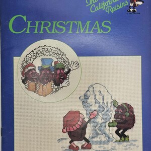 May include: A cross-stitch pattern book titled "Christmas" featuring The California Raisins. The cover is blue with green text and illustrations of the raisin characters. The book includes ten counted cross-stitch designs.
