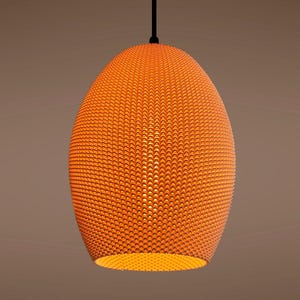 May include: Orange pendant light fixture with a textured, oval-shaped shade. The shade is covered in a pattern of small, raised dots. The light hangs from a black cord and is illuminated from within, casting a warm glow.