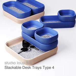 May include: Blue and beige stackable desk trays with a ribbed design. The trays have a felt insert and are shown with keys. The text "studio loup" and "Stackable Desk Trays Type 4" are visible.